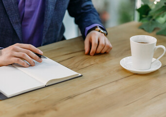 Close-up of businessman's hand with clock, notepad and cup of aromatic coffee on wooden table