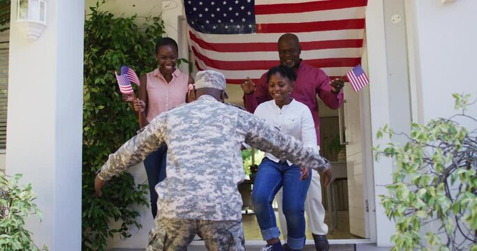 African american soldier father hugging his excited family front of house with american flag