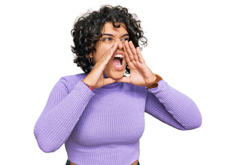 Young hispanic woman with curly hair wearing casual clothes shouting angry out loud with hands over mouth