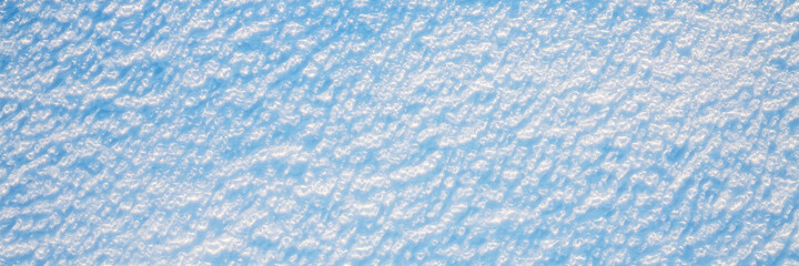 Beautiful winter background with snowy ground. Natural snow texture. Wind sculpted patterns on snow surface. Wide panoramic texture for background and design.