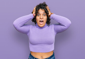 Young hispanic woman with curly hair wearing casual clothes crazy and scared with hands on head, afraid and surprised of shock with open mouth