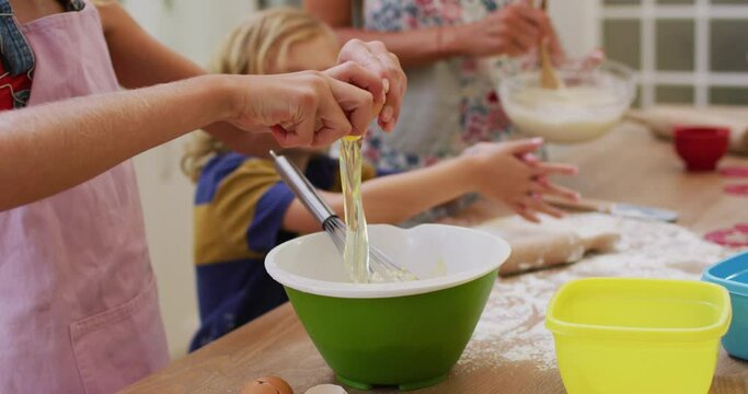 Midsection of caucasian mother in kitchen baking son and daughter breaking egg into a bowl
