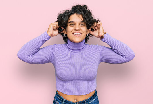 Young hispanic woman with curly hair wearing casual clothes smiling pulling ears with fingers, funny gesture. audition problem