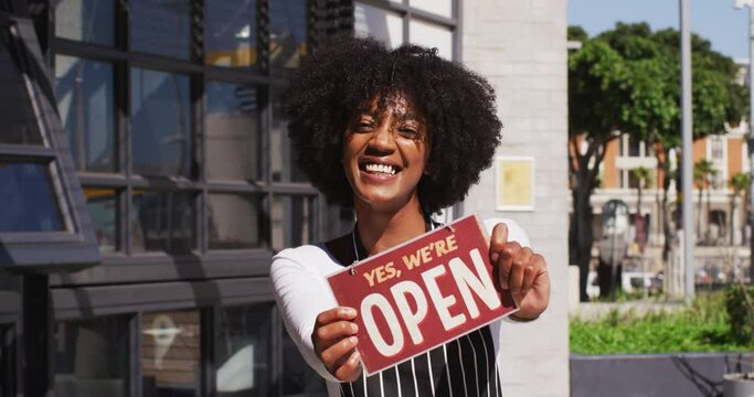 Happy african american female cafe worker showing were open signage and smiling