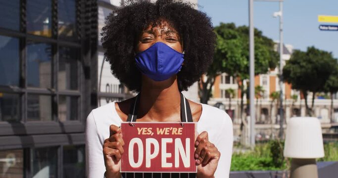 African american female cafe worker wearing face mask showing were open signage