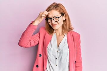 Young caucasian woman wearing business style and glasses pointing unhappy to pimple on forehead,...