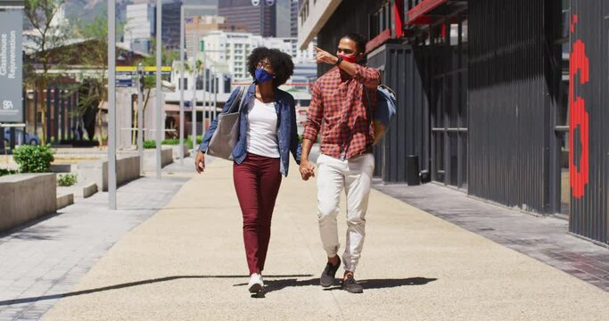 Diverse couple wearing face masks walking and holding hands