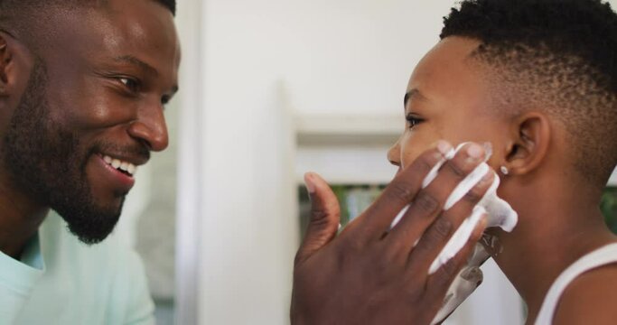 African american father putting shaving cream on his son mouth and laughing together