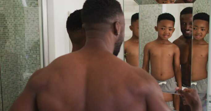 African american father and son flexing their muscles in mirror together