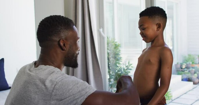 African American Father Helping His Son With Getting Dressed In Bedroom