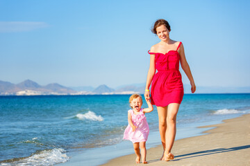 Mother and little daughter walking on the sea beach in Greece