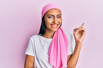 Young brunette woman wearing breast cancer support pink scarf smiling happy pointing with hand and...