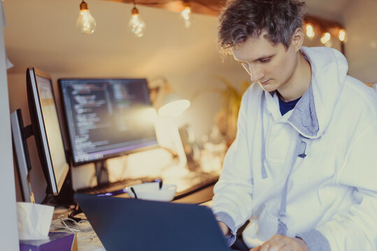 A man sitting at a desk working from home on his computer. IT specialist programmer writing code on his pc and laptop. Developer remote home office. Freelance workspace. Soft selective focus.