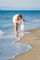 Mother and little daughter walking on the sea beach in Greece