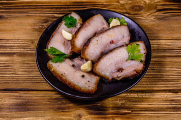 Slices of baked pork belly, garlic and parsley on a black plate