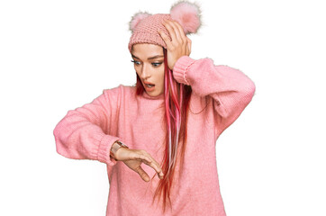 Young caucasian woman wearing casual clothes and wool cap looking at the watch time worried, afraid...