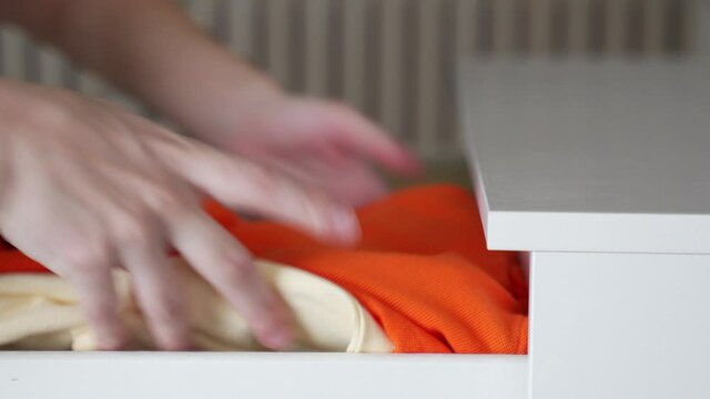 Women's hands put clothes in chest of drawers. Concept of order in the storage of things