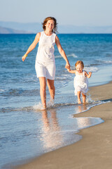 Mother and little daughter ranning on the sea beach in Greece