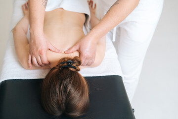 Fototapeta premium Male masseur with strong hands professionally massaging scapulas and shoulders to female client. Beautiful naked young woman with perfect skin getting relaxing back massage at spa salon.
