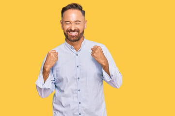 Handsome middle age man wearing business shirt excited for success with arms raised and eyes closed...