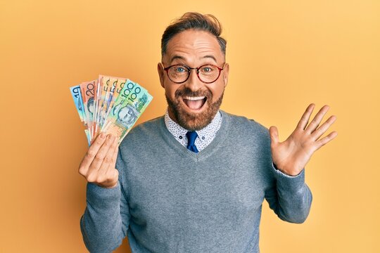 Handsome middle age man holding australian dollars celebrating achievement with happy smile and winner expression with raised hand