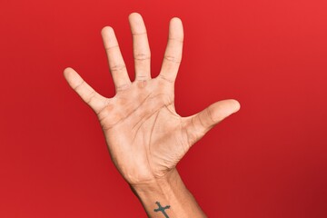 Hand of hispanic man over red isolated background counting number 5 showing five fingers