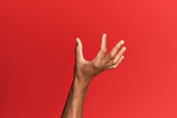 Hand of hispanic man over red isolated background picking and taking invisible thing, holding object with fingers showing space