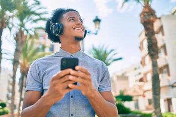 Young african american man smiling happy using smartphone and headphones at the city.