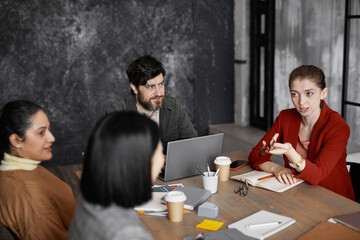 High angle view at diverse group of business people meeting at table, focus on young businesswoman wearing red jacket and sharing ideas