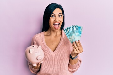 Young caucasian woman holding brazil real banknotes and piggy bank celebrating crazy and amazed for success with open eyes screaming excited.