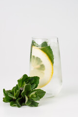 On a light background, a bunch of mint, in the background a blurred image of a chilled drink with a lemon wedge, mint leaves.