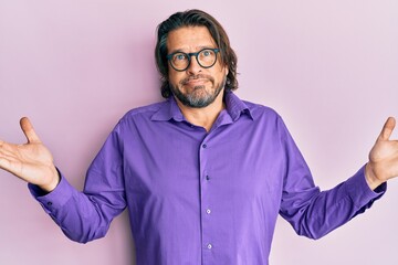 Fototapeta premium Middle age handsome man wearing casual clothes and glasses clueless and confused with open arms, no idea and doubtful face.
