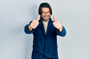 Middle age caucasian man wearing bathrobe and glasses approving doing positive gesture with hand, thumbs up smiling and happy for success. winner gesture.