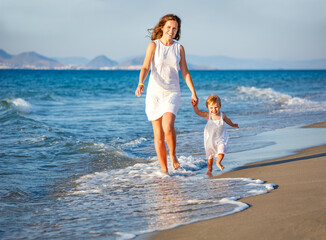 Mother and little daughter walking on the sea beach in Greece