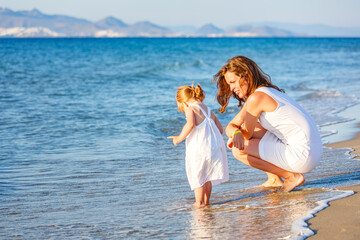 Fototapeta na wymiar Mother and little daughter playing on the sea beach in Greece