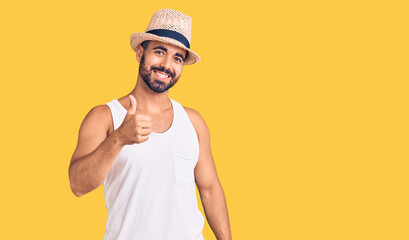 Young hispanic man wearing casual summer hat doing happy thumbs up gesture with hand. approving expression looking at the camera showing success.