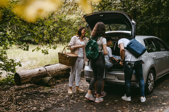 Family removing things from car trunk in forest during picnic