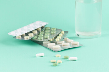 Pills and a glass of water on a mint background. Medication.