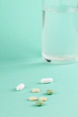Pills and a glass of water on a mint background. 