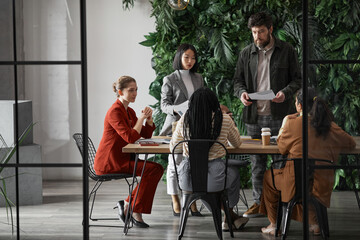 Graphic full length portrait of diverse group of business people meeting at table in modern office...