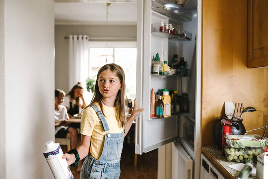 Caucasian girl with juice pack standing by refrigerator
