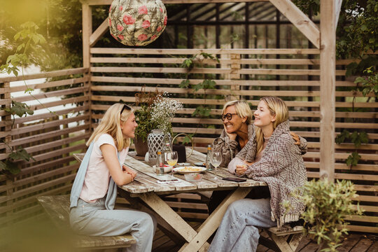 Smiling female friends spending time with grandmother at table in front yard