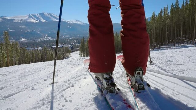 Low angle of skier clipping into a pair of skis and starts pushing off down the mountain towards a ski resort in slow motion