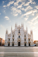 View of the Milan Cathedral with empty square due to the coronavirus blockade, with blue sky with white clouds and glow of light from the newly risen sun, vertical