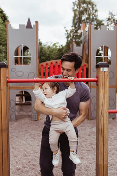 Male toddler with father hanging on monkey bar in playground