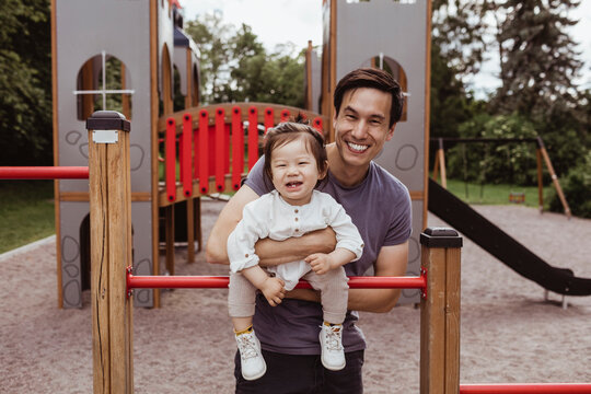 Smiling father and son leaning over monkey bar in park - Powered by Adobe