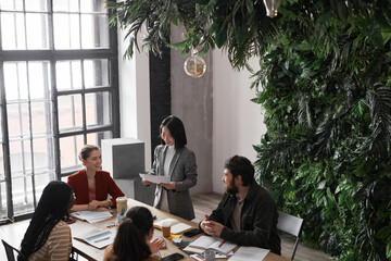 High angle portrait of diverse group of business people meeting at table in modern office interior decorated by plants, copy space