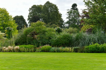 Scenic Summertime View of a Beautiful English Style Landscape Garden with a Green Mowed Lawn, Leafy Trees and Colourful Flower Bed