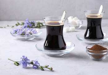 Chicory beverage in two glass cups, with concentrate and flowers on gray background. Healthy herbal beverage, coffee substitute