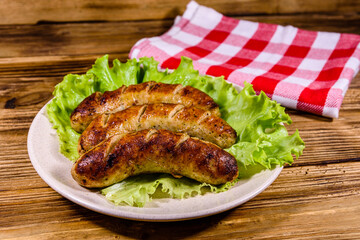 Plate with roasted sausages and lettuce leaves on a wooden table